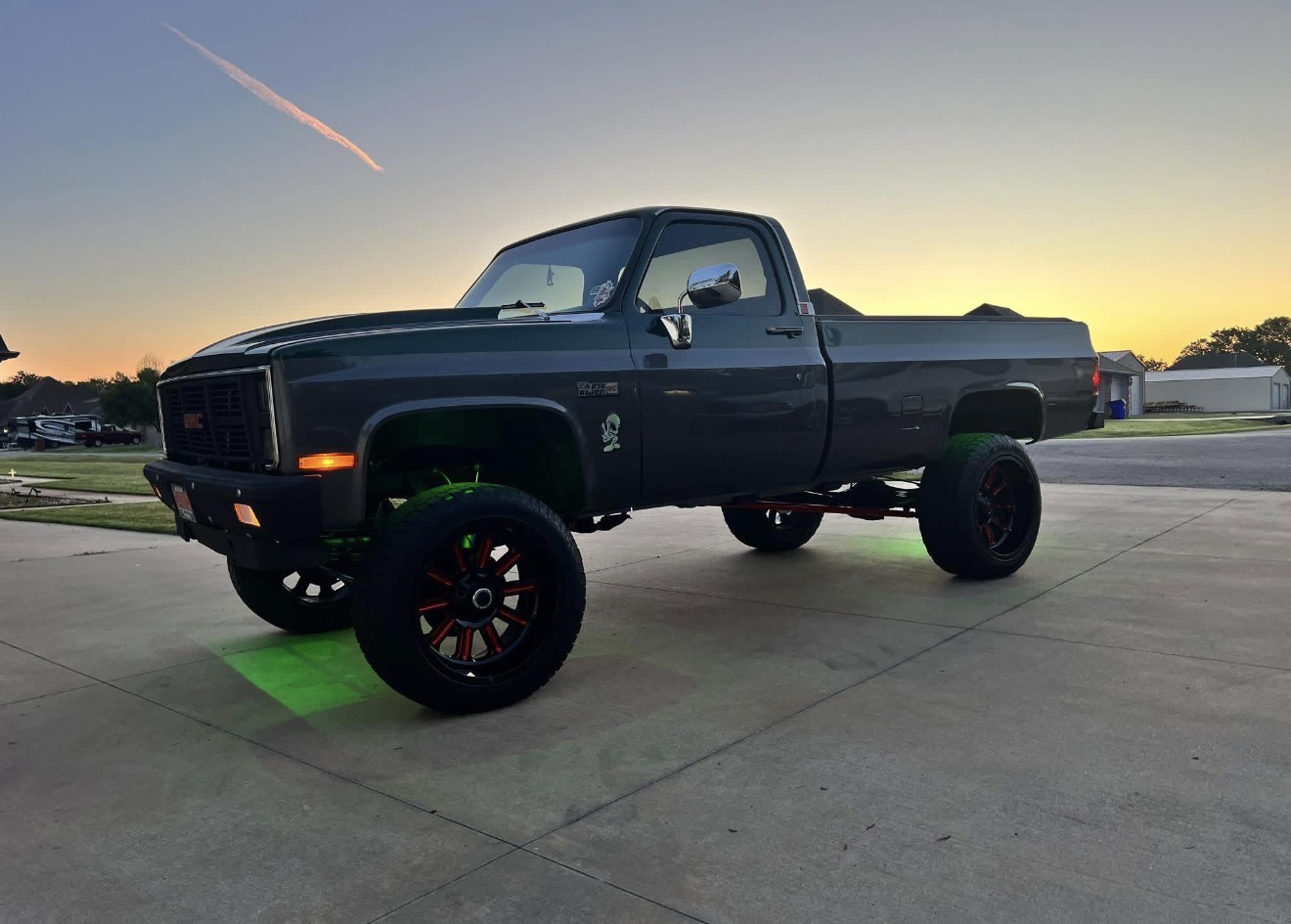Lifted square body GMC pickup on custom wheels at sunset
